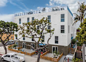 Thumbnail 23 of 28 - A white building with a balcony on the top floor is surrounded by trees and has a white van parked in front.