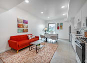 Thumbnail 4 of 28 - A red couch sits in a living room with a glass table and chairs.