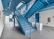 Thumbnail 25 of 28 - A blue staircase in a building with a white wall and a fire extinguisher.