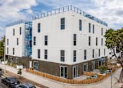 Thumbnail 1 of 28 - A white building with a blue balcony on the top floor.