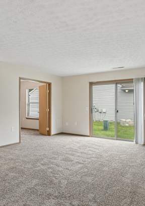 A spacious room with a carpeted floor and a sliding glass door leading to a patio.