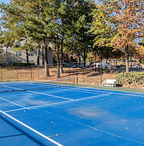 A blue tennis court surrounded by trees and a fence.