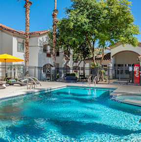 A pool with a yellow umbrella and palm trees in the background.