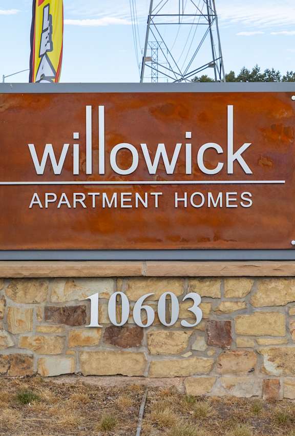A brown sign for Willowick Apartment Homes stands in front of a parking lot.
