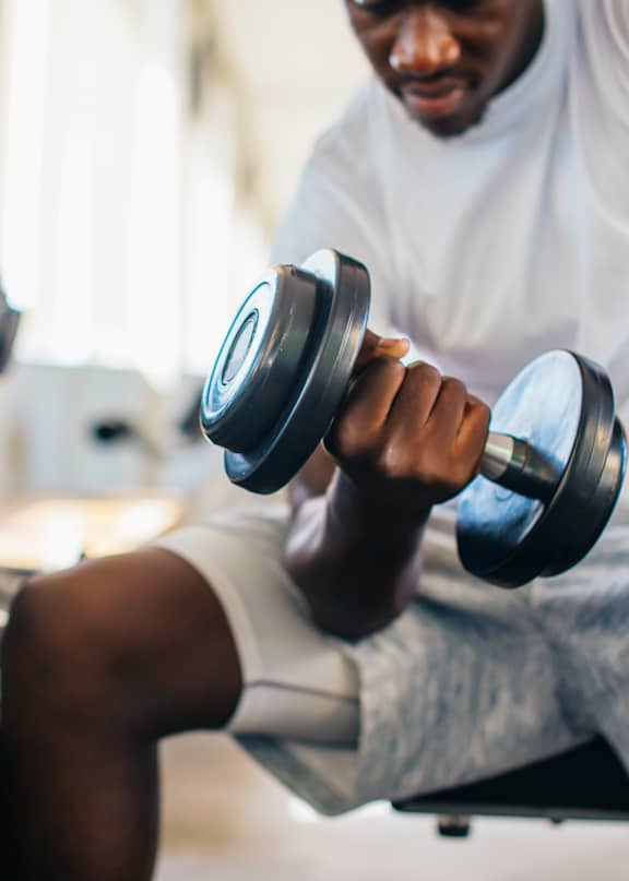 A man in a white t-shirt is running on a treadmill in a gym with other people exercising around him.