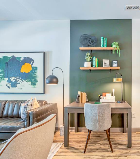 A living room with a grey sofa, a grey chair, a grey table, a green bookshelf, a painting, a lamp, and a wooden floor.