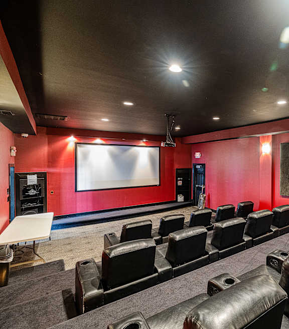 A movie theater with red walls and black leather seats.