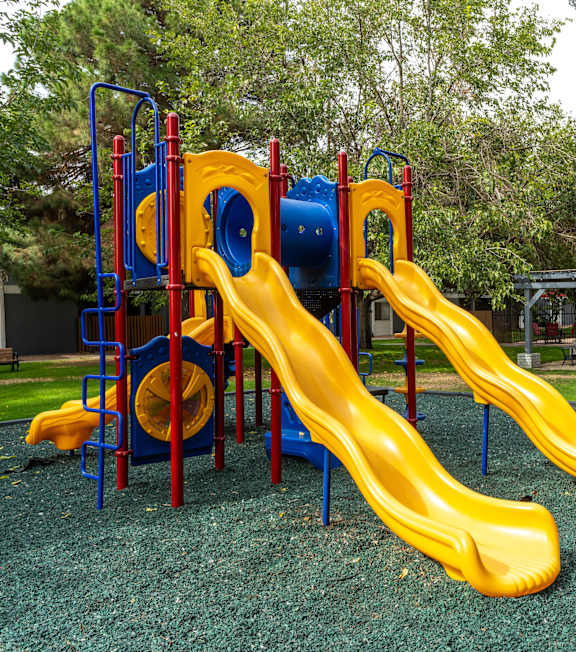 A playground with a yellow slide and a blue and red structure.