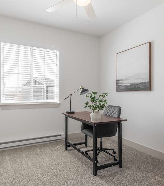 A room with a desk and chair, a plant, and a window with blinds.