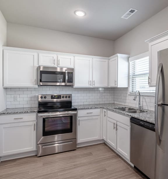 an empty kitchen with stainless steel appliances and white cabinets