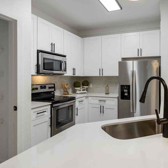 A modern kitchen with a stainless steel sink and white cabinets.