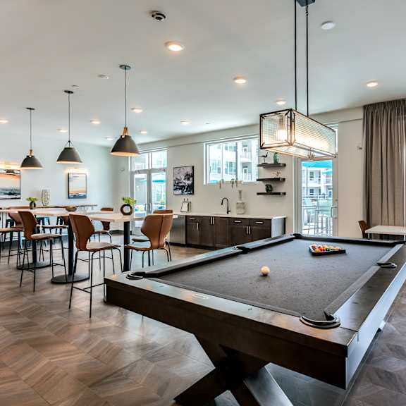 A pool table is in the middle of a room with a bar and chairs.