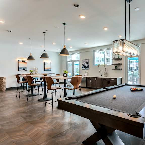 A pool table is in the middle of a room with a bar and chairs.