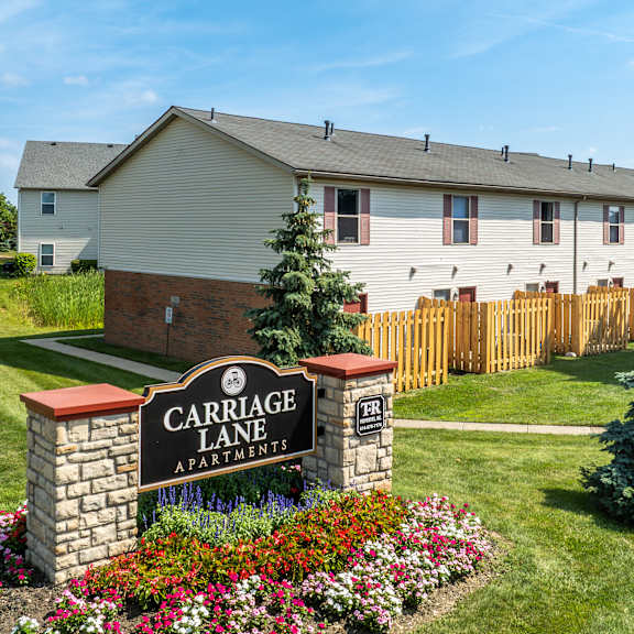 A sign for Carriage Lane Apartments is surrounded by flowers.