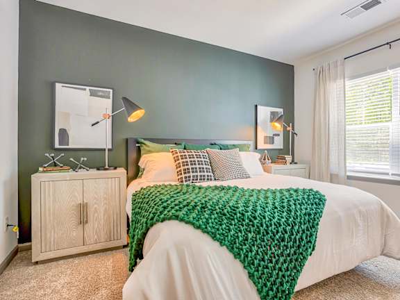 A bedroom with a white bed and a green knitted blanket.