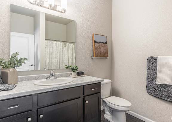 A bathroom with a white toilet, a sink with a mirror above it, and a towel rack on the wall.