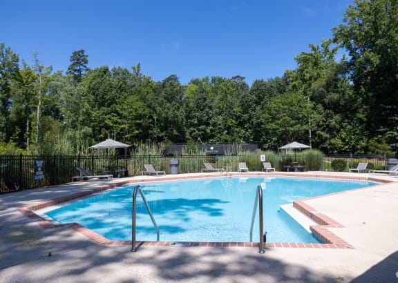 a swimming pool with chairs and trees in the background