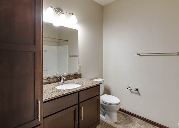 A bathroom with a toilet, sink, mirror, and a towel bar.