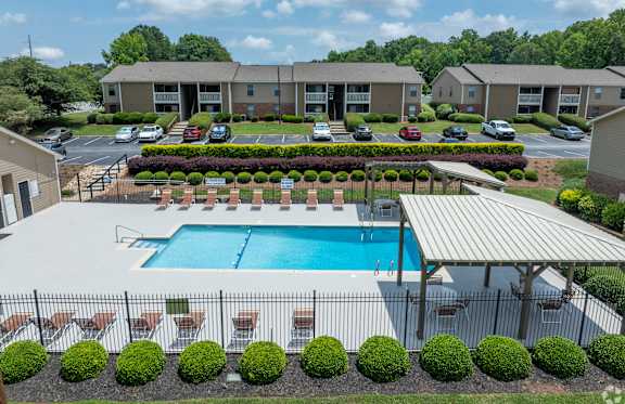 A swimming pool surrounded by a fence and bushes in front of a building.