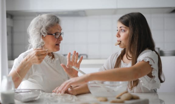 two women sitting at a table in a kitchen making cookies