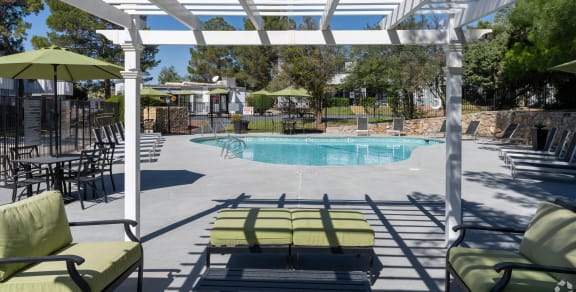 a swimming pool with chairs under a white pergola