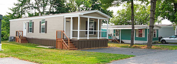 A mobile home with a porch and a car parked in the driveway.