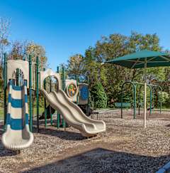 A playground with a slide and a green umbrella.