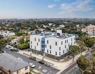 A white building with a blue glass addition sits on a street corner with cars parked on the side.