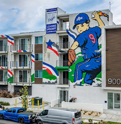 A large mural of a baseball player is on the side of a building with a sign that says "Leasing January".