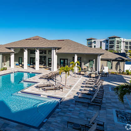 A large swimming pool in front of a building with a poolside lounge.