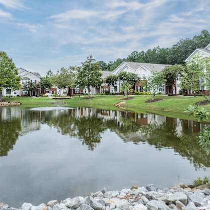 a pond with houses in the background and grass and trees at Carlton Park Apartment Homes, Flowood, MS, 39232