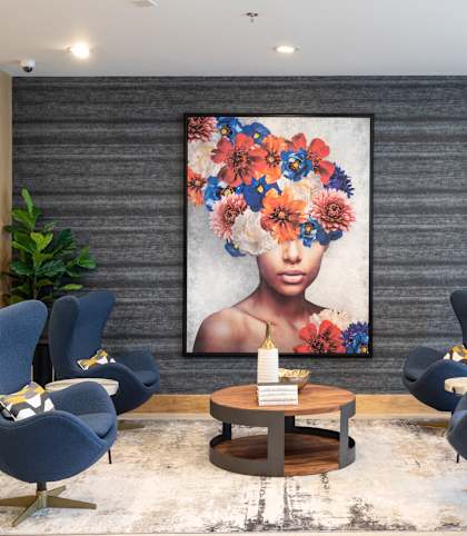 A modern living room with a large floral painting on the wall and blue armchairs.