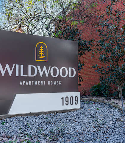 A sign for Wildwood Apartment Homes is displayed in front of a brick building.