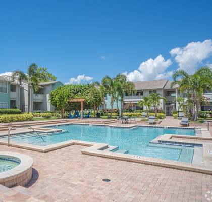 A swimming pool surrounded by a brick patio and a small fountain in the middle.