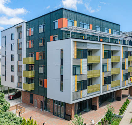 A modern multi-story building with balconies and a mix of grey, yellow, and orange colors.