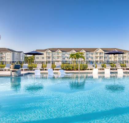 A large swimming pool in front of a resort with palm trees.