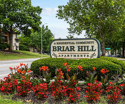 A sign for Briar Hill Apartments is surrounded by red flowers.