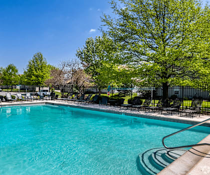 A large swimming pool surrounded by trees and chairs.
