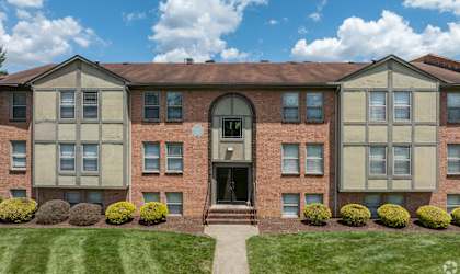 front view of a brick apartment building with green grass and shrubs
