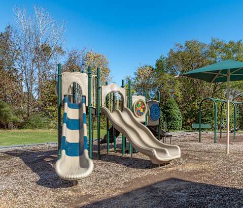 A playground with a slide and a green umbrella.