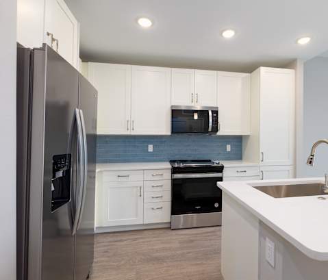 A modern kitchen with a stainless steel refrigerator and white countertops.at Imperial Crossing Luxury Apartment Homes, Bonita Springs
