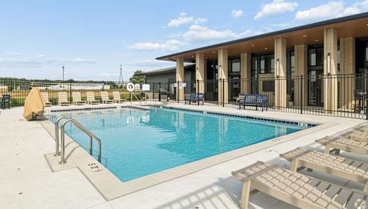 A pool with sun loungers and a building in the background.