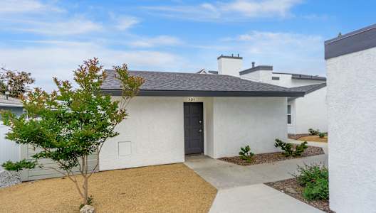 A white house with a black door and a small tree in front. at Hamilton Courtyard Apartments, Costa Mesa, CA, 92627