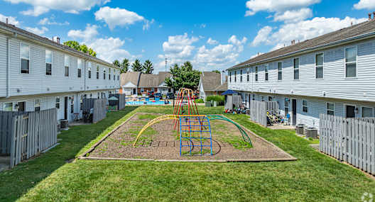 A playground with a swing set in the middle of a grassy area surrounded by apartment buildings.