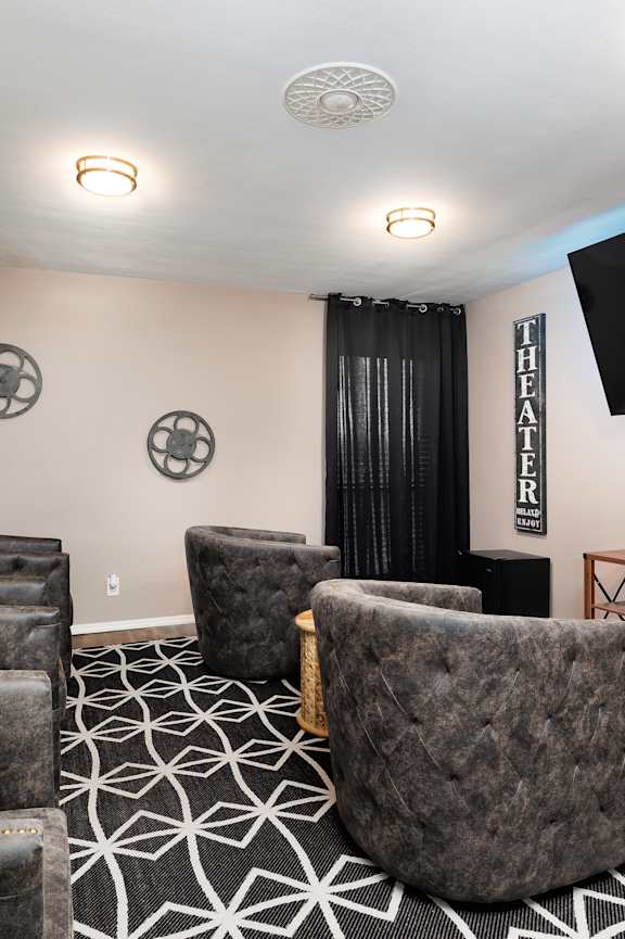 A living room with a large grey chair in the center and a flat screen TV mounted on the wall.