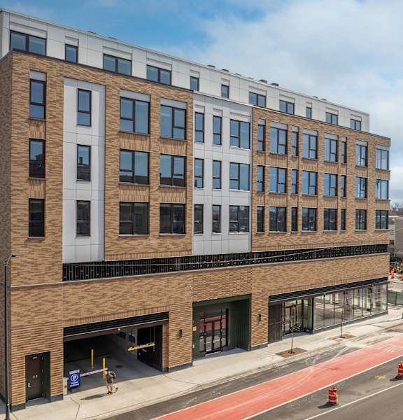 A modern building with a mix of brick and panel construction is situated on a busy street corner.