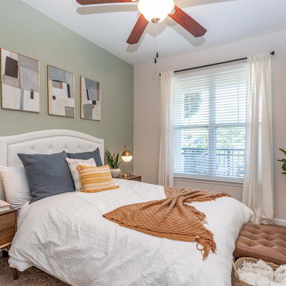 A bedroom with a bed, nightstand, and a plant.