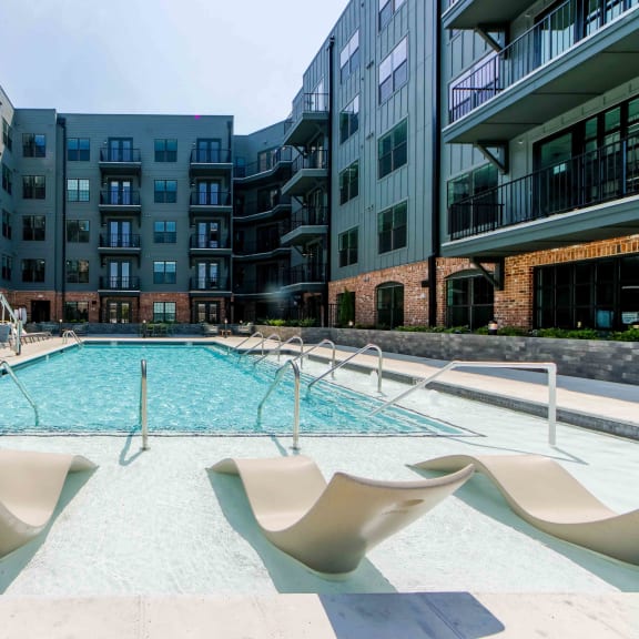 an outdoor pool with lounge chairs next to an apartment building