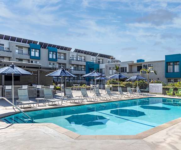 a swimming pool with chairs and umbrellas in front of an apartment building