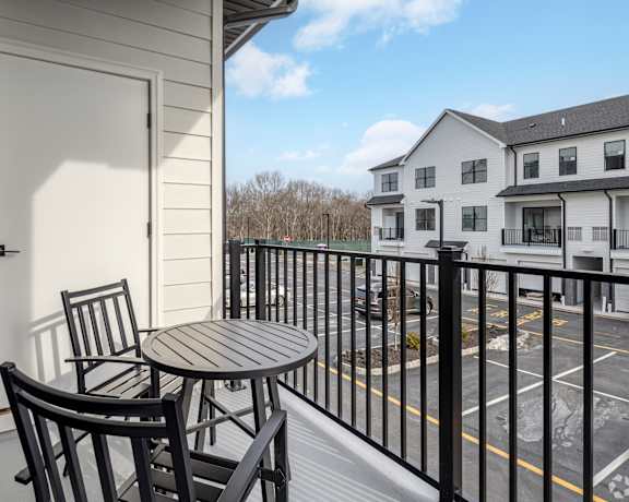A balcony with a table and chairs overlooks a parking lot.